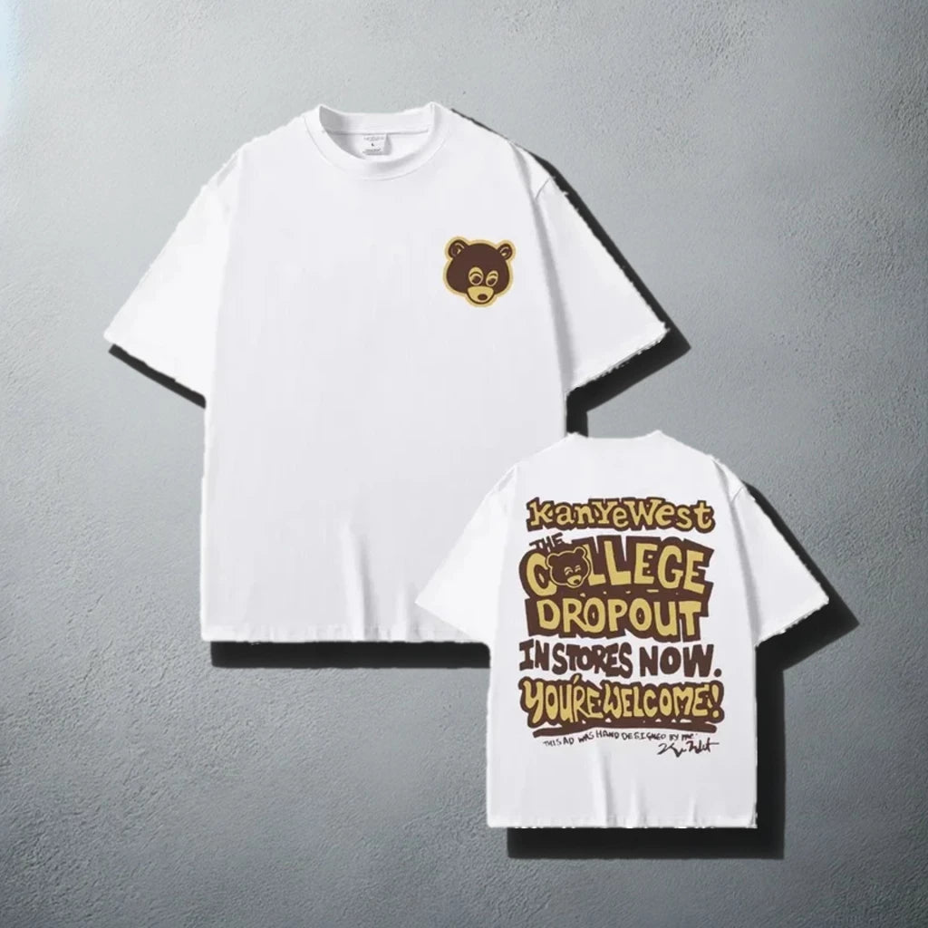 A stylish white t-shirt, featuring a small brown bear logo on the front left chest area and a bold graphic on the back that reads 'Kanye West The College Dropout In Stores Now. You're Welcome!' with a playful font design, reminiscent of Kanye West's debut album promotional material.