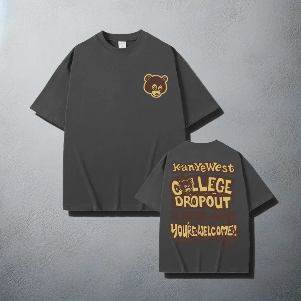 A stylish dark gray t-shirt, featuring a small brown bear logo on the front left chest area and a bold graphic on the back that reads 'Kanye West The College Dropout In Stores Now. You're Welcome!' with a playful font design, reminiscent of Kanye West's debut album promotional material.