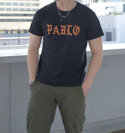 Man wearing a black 'PABLO' T-shirt with orange lettering, casual streetwear style inspired by Kanye West