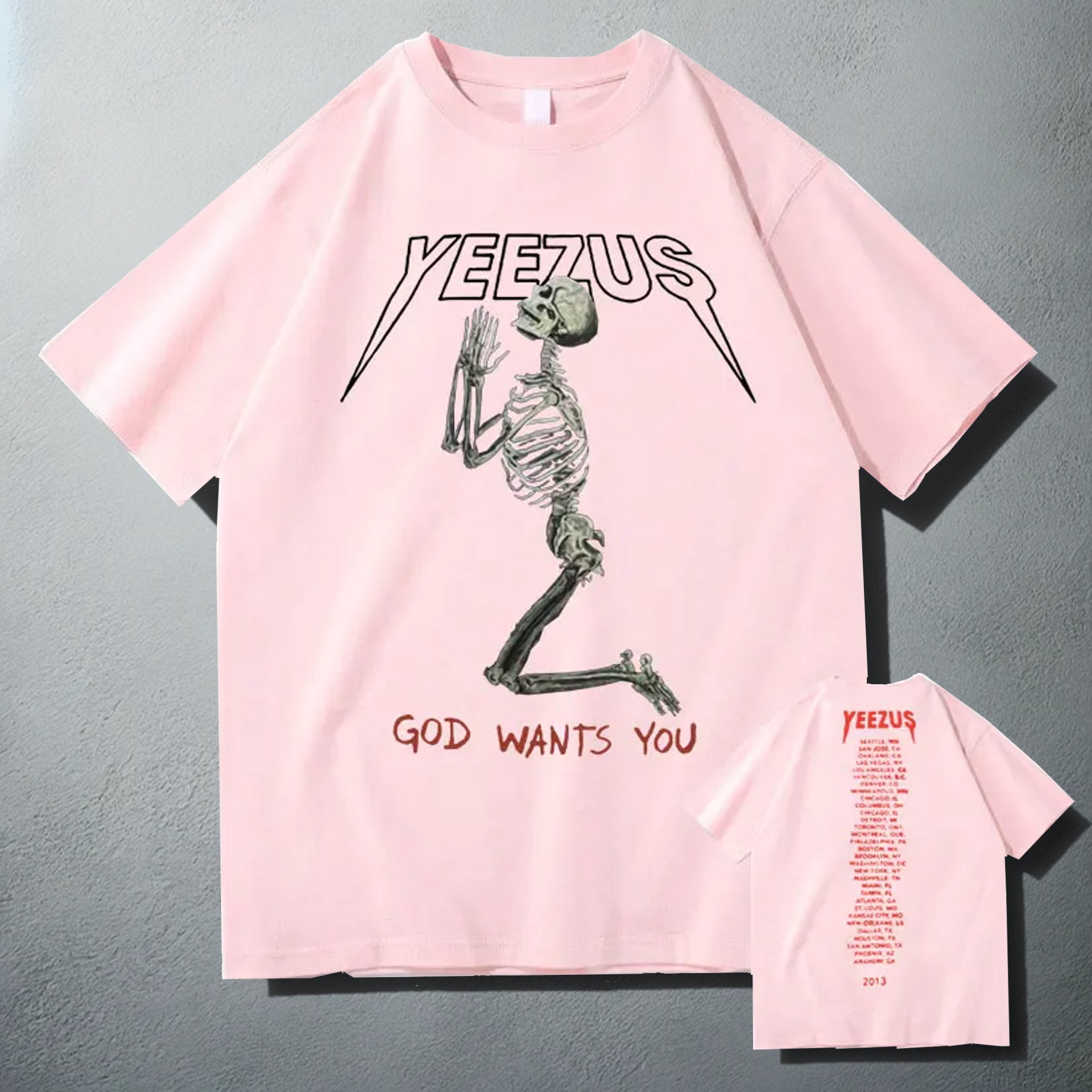 Pink 'Yeezus' T-shirt with a white praying skeleton graphic and 'God Wants You' text, showcasing a bold design inspired by Kanye West's album